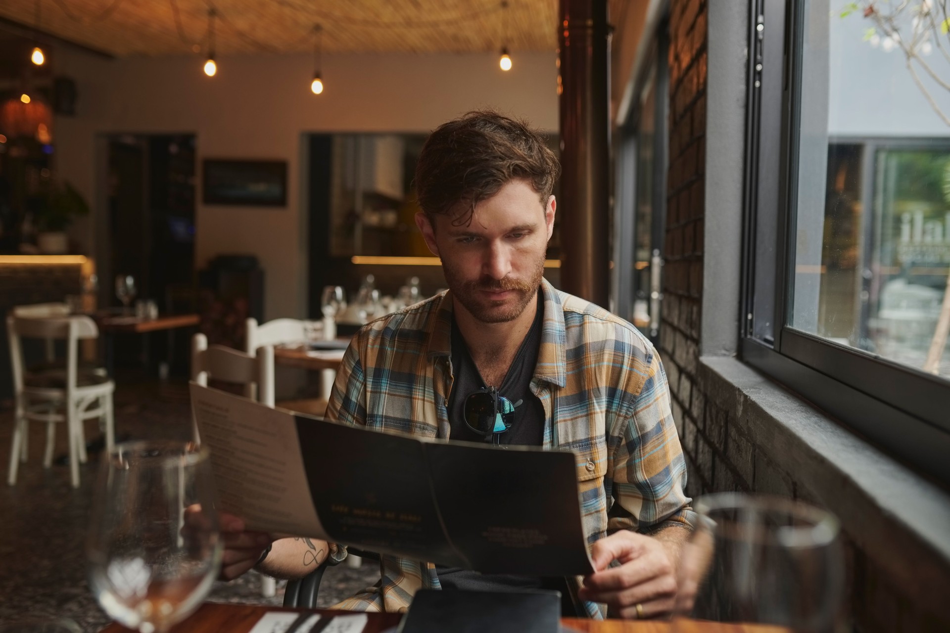 Hombre, restaurante y menú de lectura para la elección de alimentos, la decisión y el descuento en una pequeña empresa en Europa. Persona joven o cliente con carta de vinos, información y servicios para almorzar en mesa en una cafetería